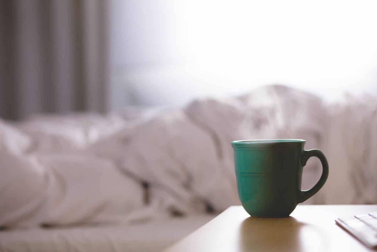 Kaffeetasse auf Nachtisch vor einem Bett