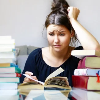 Junge Studentin verzweifelt beim lernen, sie ist umgeben von Büchern