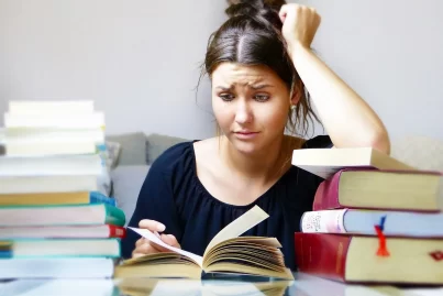 Junge Studentin verzweifelt beim lernen, sie ist umgeben von Büchern