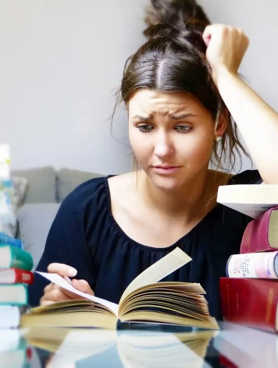 Junge Studentin verzweifelt beim lernen, sie ist umgeben von Büchern