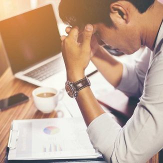 Mann am Arbeitsplatz im Büro. Er wirkt gestresst und nachdenklich.