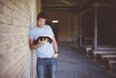 Mann steht in einer leeren Halle und liest ein Buch.