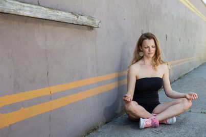 Hippes Mädchen meditiert vor einer urbanen Betonmauer