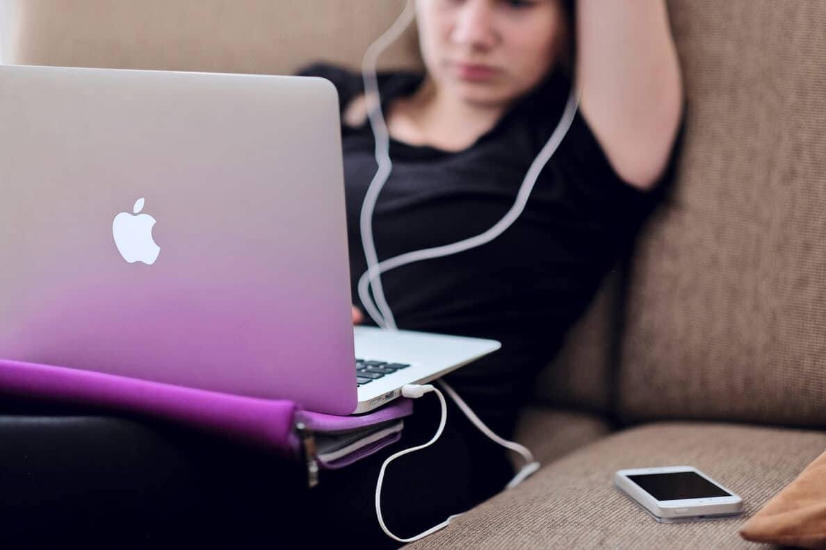 Studentin sitzt mit ihrem MacBook auf dem Schoß auf dem Sofa