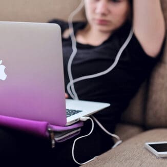 Studentin sitzt mit ihrem MacBook auf dem Schoß auf dem Sofa