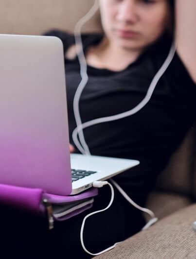 Studentin sitzt mit ihrem MacBook auf dem Schoß auf dem Sofa