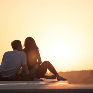 Mann und Frau sitzen und sehen sich den Sonnenuntergang an