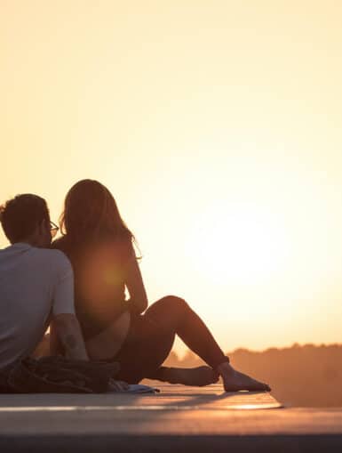 Mann und Frau sitzen und sehen sich den Sonnenuntergang an