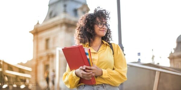 Frau in gelber Jacke, die vor historischem Gebäude rotes Buch hält