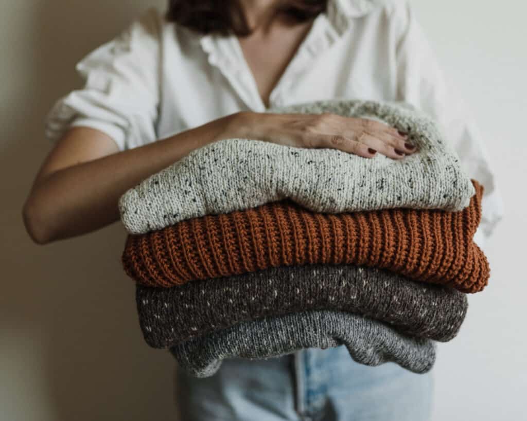 Hände einer jungen Frau mit einem Stapel Secondhand-Pullover, die den Secondhand-Trend widerspiegelt