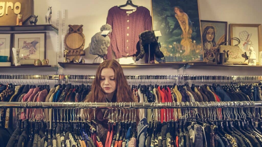 Junge Frau, die dem Secondhand-Trend folgt und Secondhand-Kleidung in einem Laden durchsieht