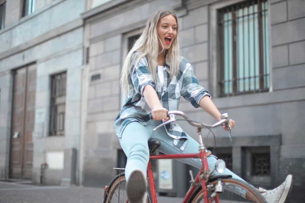 Studentin auf rotem älterem Fahrrad streckt beim Fahren die Füße in die Luft. Neuen Studienort kennenlernen!