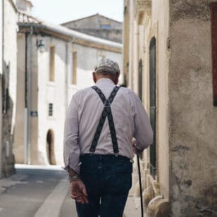 Pensionsvorsorge - Alter Mann von hinten der auf einer gepflasterten Straße geht, links und recht Häuser