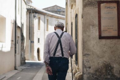 Pensionsvorsorge - Alter Mann von hinten der auf einer gepflasterten Straße geht, links und recht Häuser