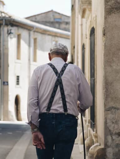Pensionsvorsorge - Alter Mann von hinten der auf einer gepflasterten Straße geht, links und recht Häuser