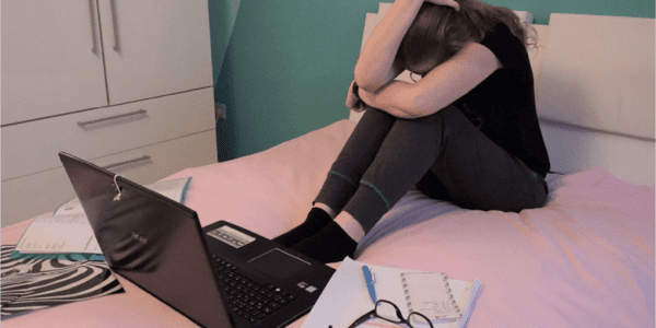 Frau die mit Laptop und Lernunterlagen verzweifelt auf einem Bett sitzt
