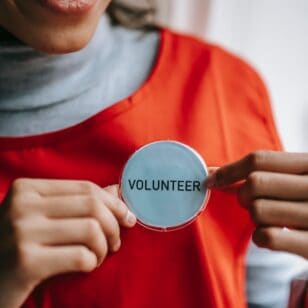 Frau mit rotem T-Shirt steckt sich einen Button auf dem Freiwilligenarbeit steht an.