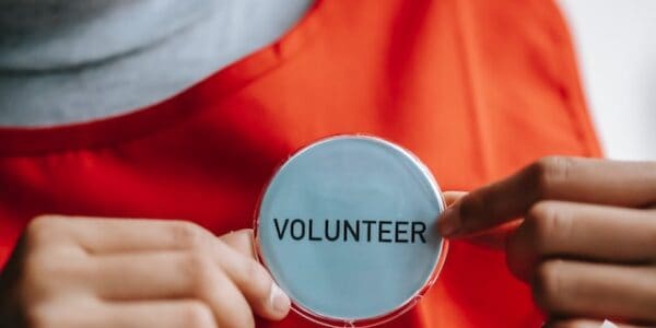 Frau mit rotem T-Shirt steckt sich einen Button auf dem Freiwilligenarbeit steht an.