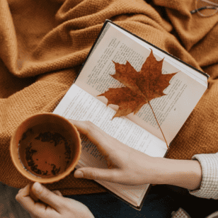 Tasse mit Heißgetränk und Buch mit Herbstblatt