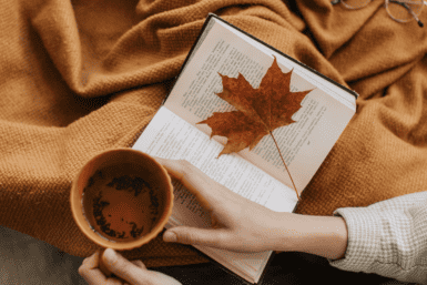 Tasse mit Heißgetränk und Buch mit Herbstblatt