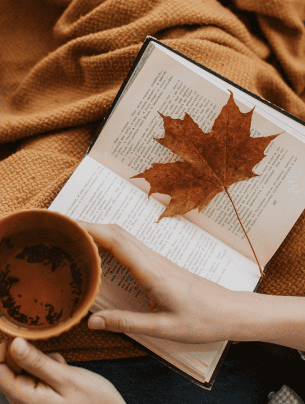 Tasse mit Heißgetränk und Buch mit Herbstblatt