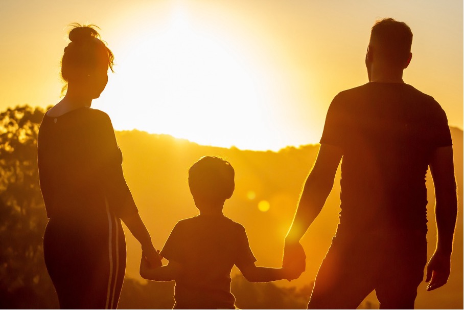 Zwei Eltern und ihr Kind schauen auf den Sonnenuntergang zu