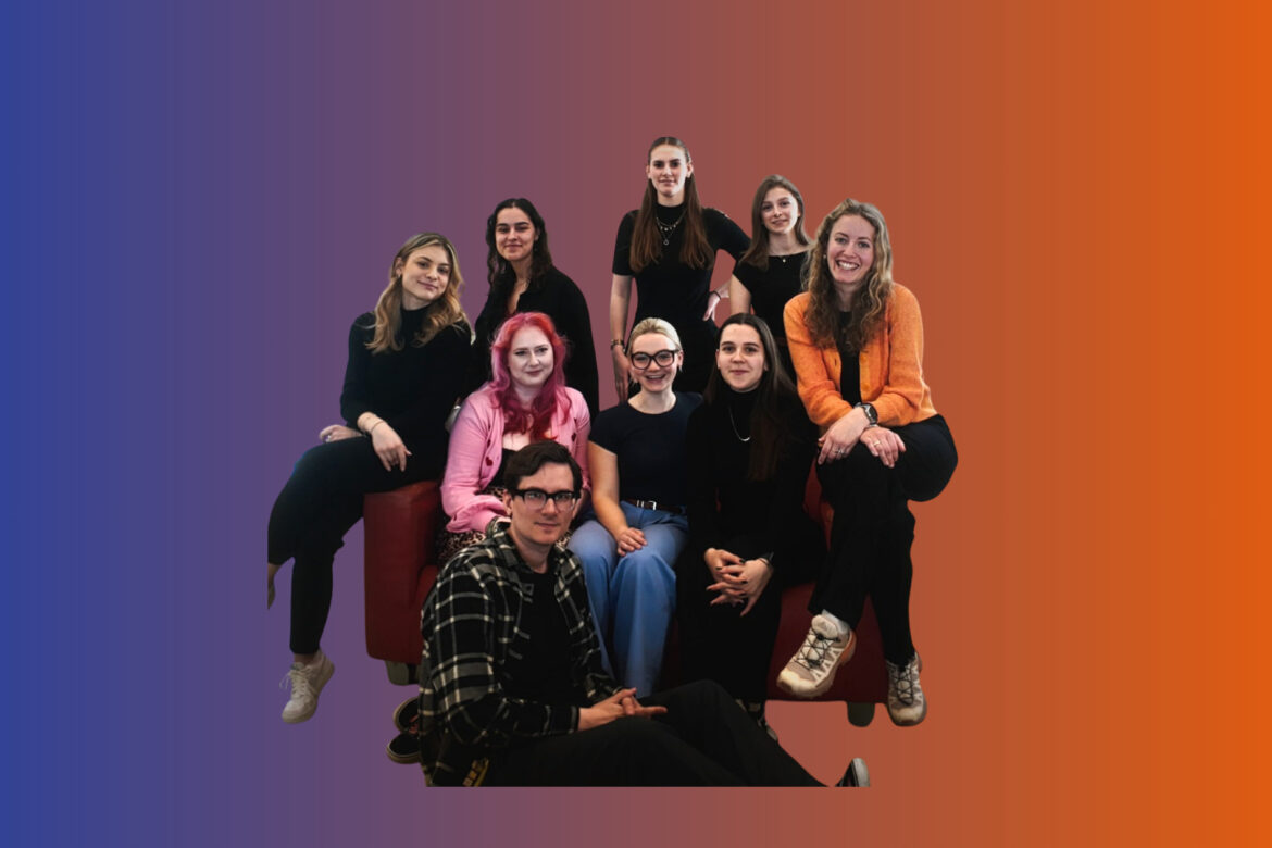 Das neue SOFA Team 2025 auf einem roten Sofa. Im Hintergrund sind die Farben der CI zu erkennen: blau und orange.