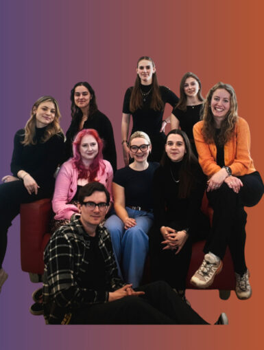 Das neue SOFA Team 2025 auf einem roten Sofa. Im Hintergrund sind die Farben der CI zu erkennen: blau und orange.