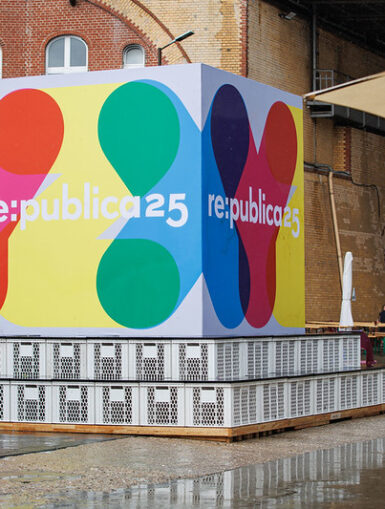 Frau mit Regenschirm steht vor dem Eingang der re:publica, im Hintergrund das bunte Veranstaltungsschild.