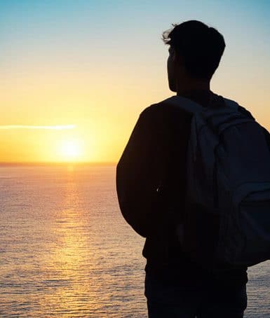 Bild eines Studenten vor einem Sonnenuntergang am Meer / KI generiert mit Adobe Express