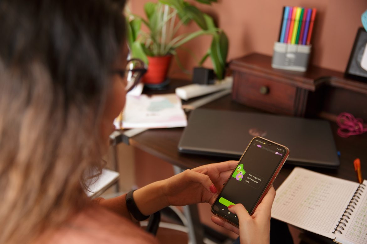 Eine junge Frau beugt sich über ihr Handy, auf dem sie gerade mithilfe der Sprachenapp Duolingo eine Sprache lernt. (c)Duolingo