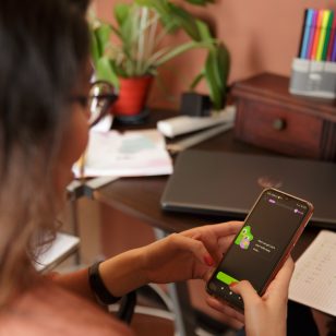 Eine junge Frau beugt sich über ihr Handy, auf dem sie gerade mithilfe der Sprachenapp Duolingo eine Sprache lernt. (c)Duolingo
