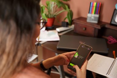 Eine junge Frau beugt sich über ihr Handy, auf dem sie gerade mithilfe der Sprachenapp Duolingo eine Sprache lernt. (c)Duolingo