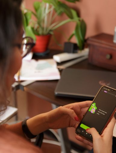 Eine junge Frau beugt sich über ihr Handy, auf dem sie gerade mithilfe der Sprachenapp Duolingo eine Sprache lernt. (c)Duolingo